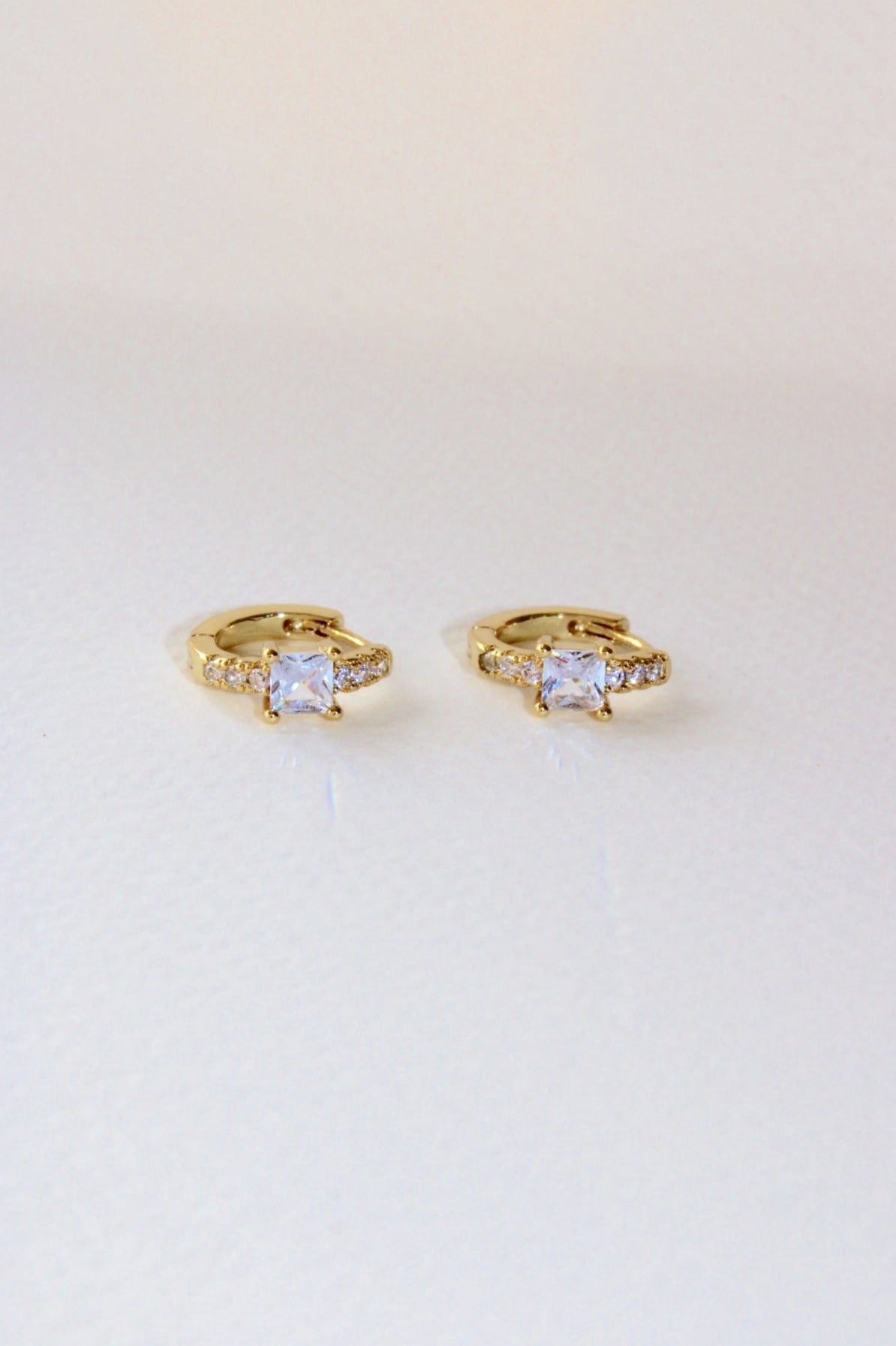 real 18k gold plated small Huggies with square central cubic zirconia at the centre of the earrings, and mini cubic zirconias surrounding it.